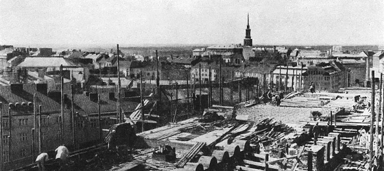 Ett svartvitt fotografi från Riksdagshusets tak. En öppen vy över Helsinki.