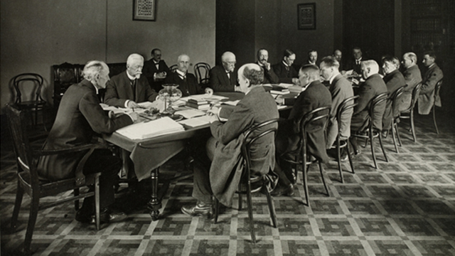 Perustuslakivaliokunta kokoontuu Säätytalolla 1918. Pöydän päässä puheenjohtaja professori K.J. Ståhlberg, vapaaherra R.A. Wrede, valiokunnan sihteeri Hjalmar Kahelin (takapöydässä), professori Ernst Estlander, professori G.G. Rosenqvist, rovasti A.O. Wuorimaa, kirjailija Santeri Alkio, toimittaja Antti Juutilainen, opettaja J.P. Kokko, toimittaja Eero Erkko, tohtori Tekla Hultin (pöydän päässä), maanviljelijä P. Pennanen, maanviljelijä E. Tukia, rovasti W. Malmivaara, rovasti F.W. Bergroth, maanviljelijä O. Rantasalo, maanviljelijä J.E. Antila, professori Lauri Ingman.